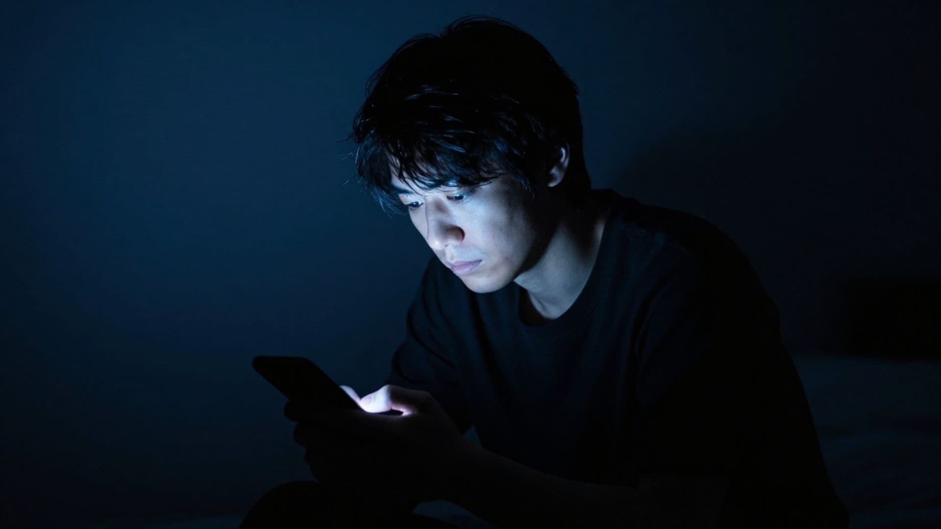 暗闇でスマートフォンを見る男性